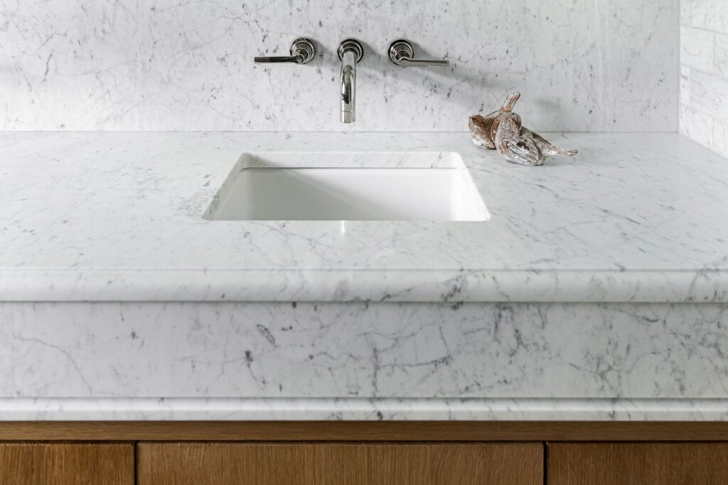 Marble sink with silver faucet on a wooden cabinet. Driftwood decoration on the countertop. Clean, minimalist bathroom design.