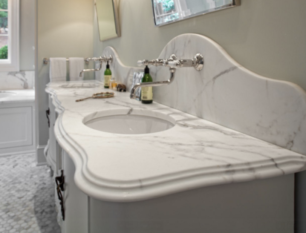 Elegant bathroom with a marble countertop and twin sinks. Mirrors, toiletries, and a towel rack in the background. Soft, neutral tones.