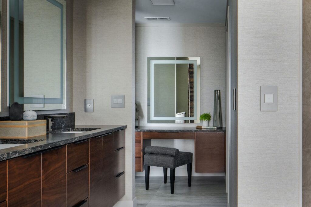 Modern bathroom with dark wood cabinets and marble countertop. Features a double sink, mirrors, and a small vanity with stool, in neutral tones.
