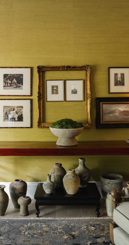 Art-filled room with framed photos, ornate mirror, and vintage vases on a black table. A peaceful, classic vibe prevails.