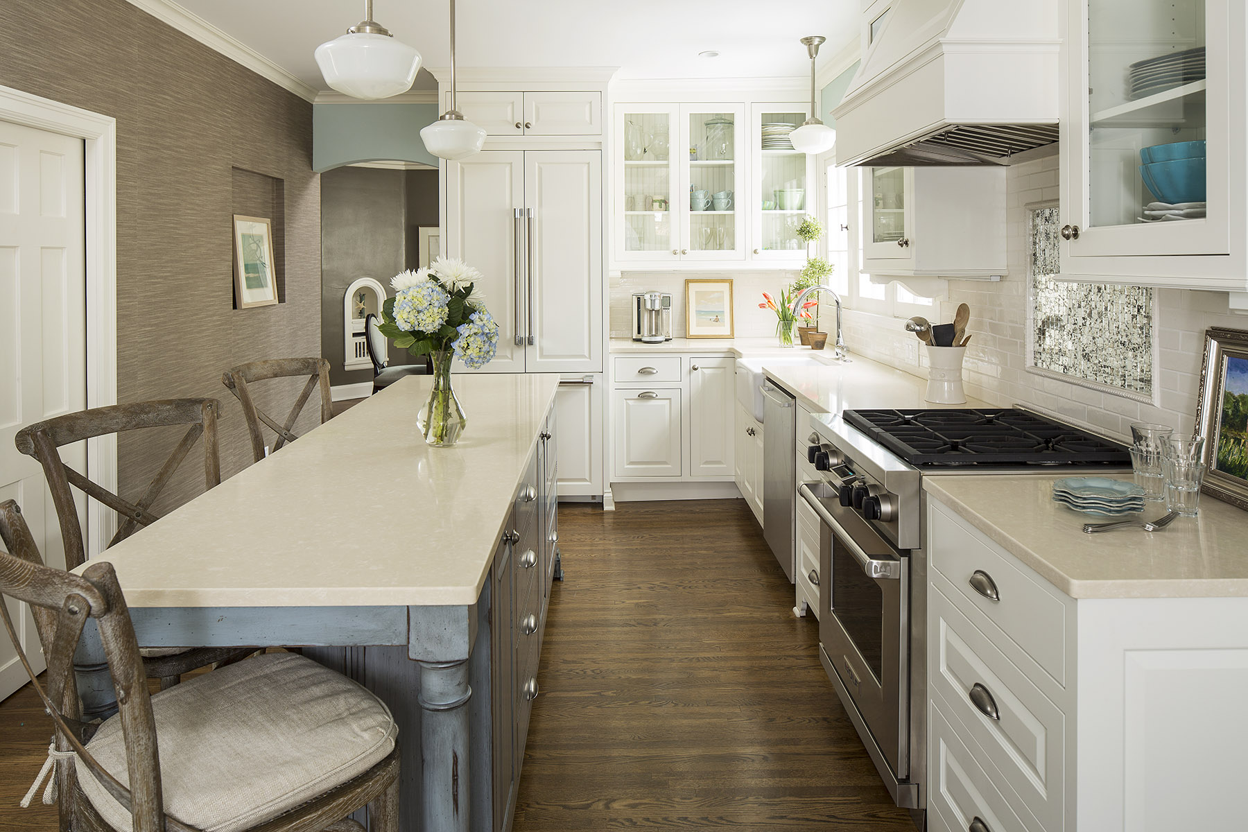 Bright kitchen with white cabinets, a long countertop, stainless steel appliances, and a vase of flowers. Wooden chairs and hardwood floors.