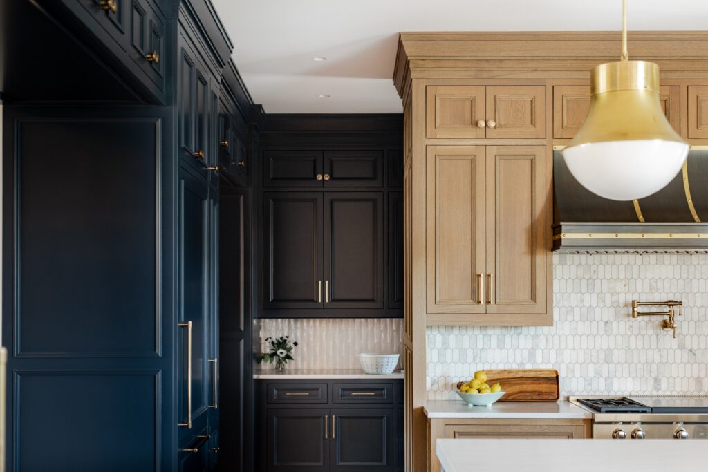 Modern kitchen with navy and wood cabinets, a white tile backsplash, gold fixtures, and a pendant light. A bowl of lemons adds color.