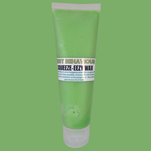 A tube of Zest Behaviour Squeezy Wax from The Cheeky Blend, standing upright against a matching green background with bold wh
