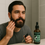 Thumbnail: A man with a full beard applies Man Glaze beard oil while looking in the bathroom mirror. The amber bottle of Man Glaze 'The
