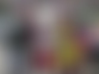 Santa and two women in festive hats stand outside a decorated vehicle with donation buckets. Overcast sky and buildings in the background.