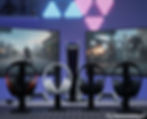 Multiple gaming headsets displayed with a PS5 console and two gaming monitors in the background, showcasing audio options for console gamers