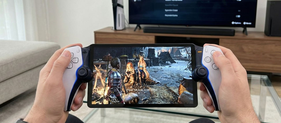 Man holding a PlayStation Portal handheld while a TV in the background shows a PS5 Pro and Xbox Series X setup.