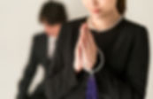 喪服を着た人が数珠を持ち祈りを捧げている