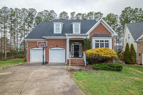 A charming brick home with a black shingle roof, two garage doors, a basketball hoop, and 