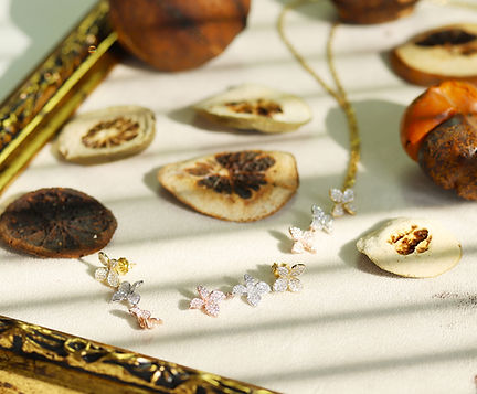 Floral necklace featuring sparkling diamond-like accents on a gold chain, displayed on a table with dried citrus slices and natural decorative elements.