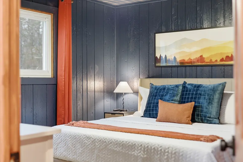 Modern rustic bedroom with dark shiplap walls, two beds with blue plaid pillows, and mountain view artwork in Pocono rental