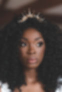 Black bride with long curly hair wears a statement wedding headpiece featuring spires of pearls and gold crystals.