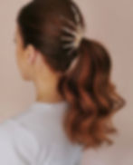 Photo shows the back of an auburn haired model's head. The model has her long hair styled in an elegant waved ponytail, accessorised with the SUNNY ponytail hair accessory from Glorious by Heidi. SUNNY is fixed to the base of the ponytail and radiates upwards and outwards through the hair like the sun's rays. 