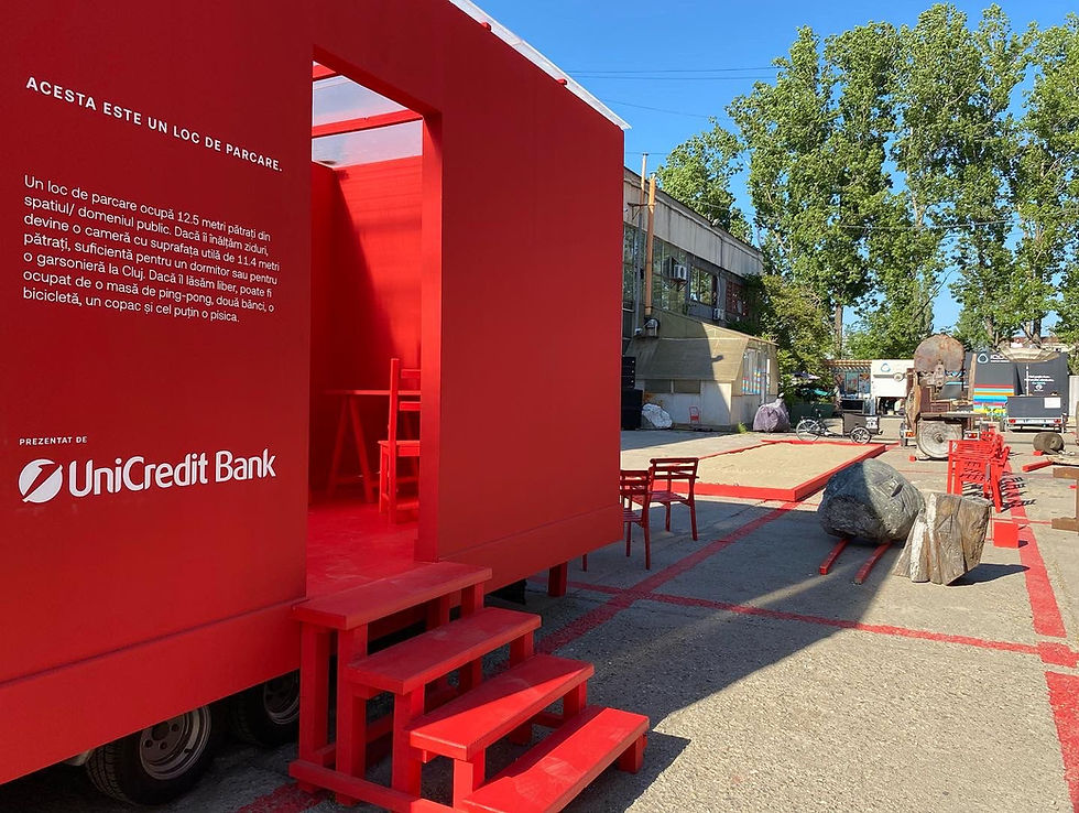 Red structure with a text about parking by UniCredit Bank, surrounded by red chairs and rocks in an outdoor setting with trees.