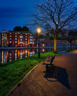 A bench and a tree on Exeter Quay at dusk with the lights of buildings in the background