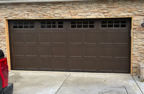 Dark brown garage door with window panels on a residential garage with a stone facade