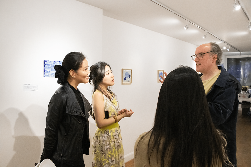 Four people engaged in conversation at an art gallery, with paintings in the background. The scene is well-lit and lively.