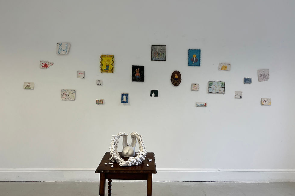 White gallery wall with small colorful artworks; a white shell-like sculpture sits on a dark wooden table in front.