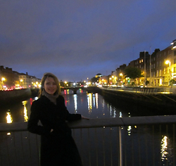 Lana standing on a bridge over the River Liffey in Dublin, with the illuminated city at night behind her.