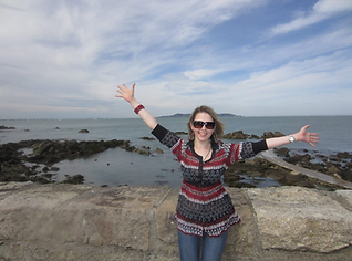 Lana sitting on a seawall on the Dun Laoghaire waterfront, facing the photographer with her arms outstretched.