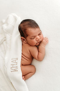 A Newborn baby laying on his tummy on a white blanket, hand tucked resting under chin