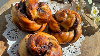 Nutellakränzchen (Germteig), auf Tortenspitze am Holzteller. weiße Blüten