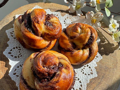Nutellakränzchen (Germteig), auf Tortenspitze am Holzteller. weiße Blüten