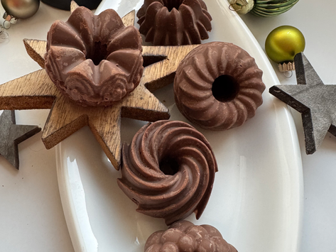 kleine Lebkuchenguglhupf mit weihnachtlicher Deko auf weißem Teller. Schwarzes Teelicht im Häuserdesign im Hintergrund. Weihnachtskugeln und Sterne