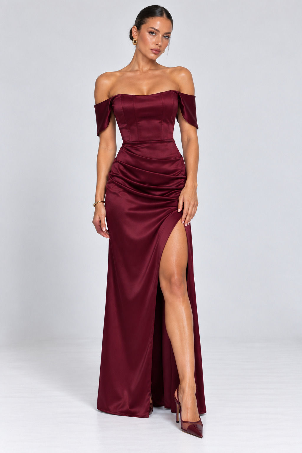 Burgundy satin off-shoulder corset maxi dress with high thigh slit, ruched waist and floor-length skirt.