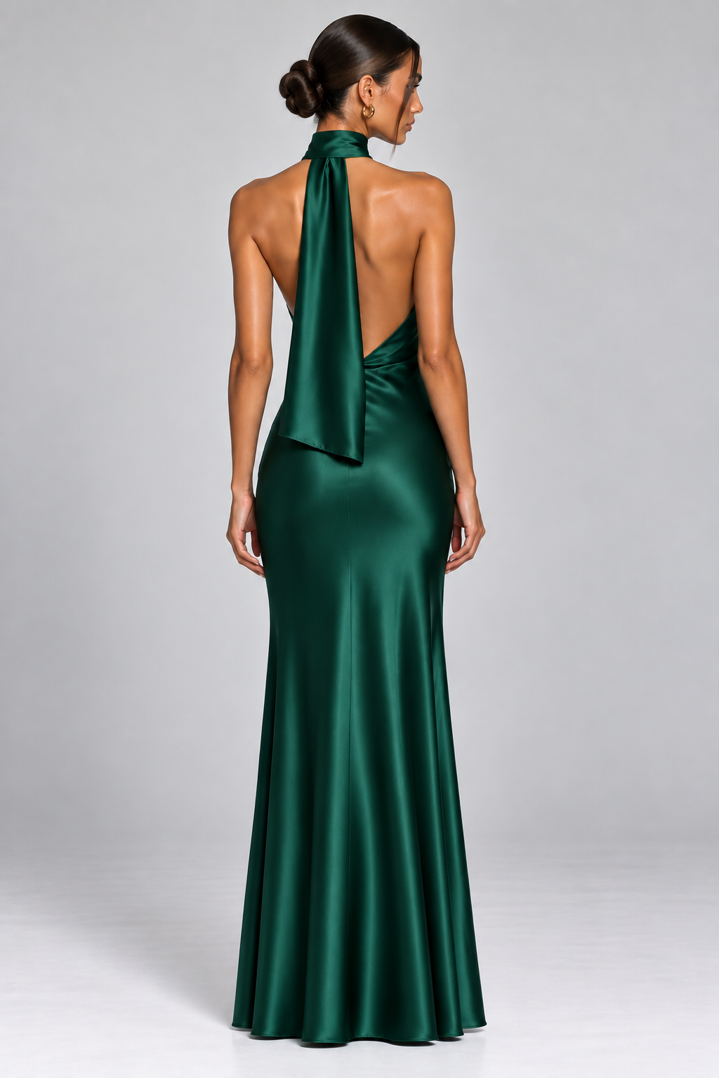Emerald green satin halter neck maxi dress with asymmetric neckline, fitted silhouette and floor-length skirt.