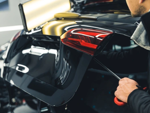 Homem realizando o serviço de remoção de mossas com ferramentas específicas, aplicando a técnica PDR (paintless dent repair) no porta malas de um carro preto.
