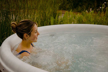 A woman relaxing in an outdoor hot tub, surrounded by lush greenery, enjoying a peaceful natural setting.