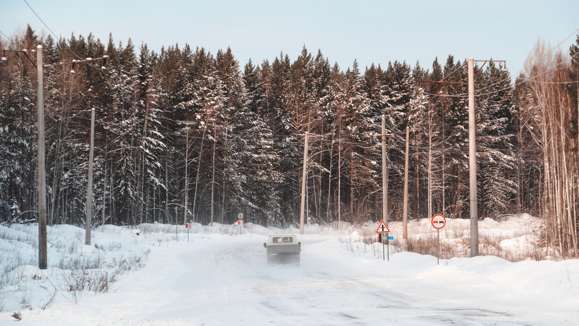 A car on a snowy road through a winter forest in Russia.