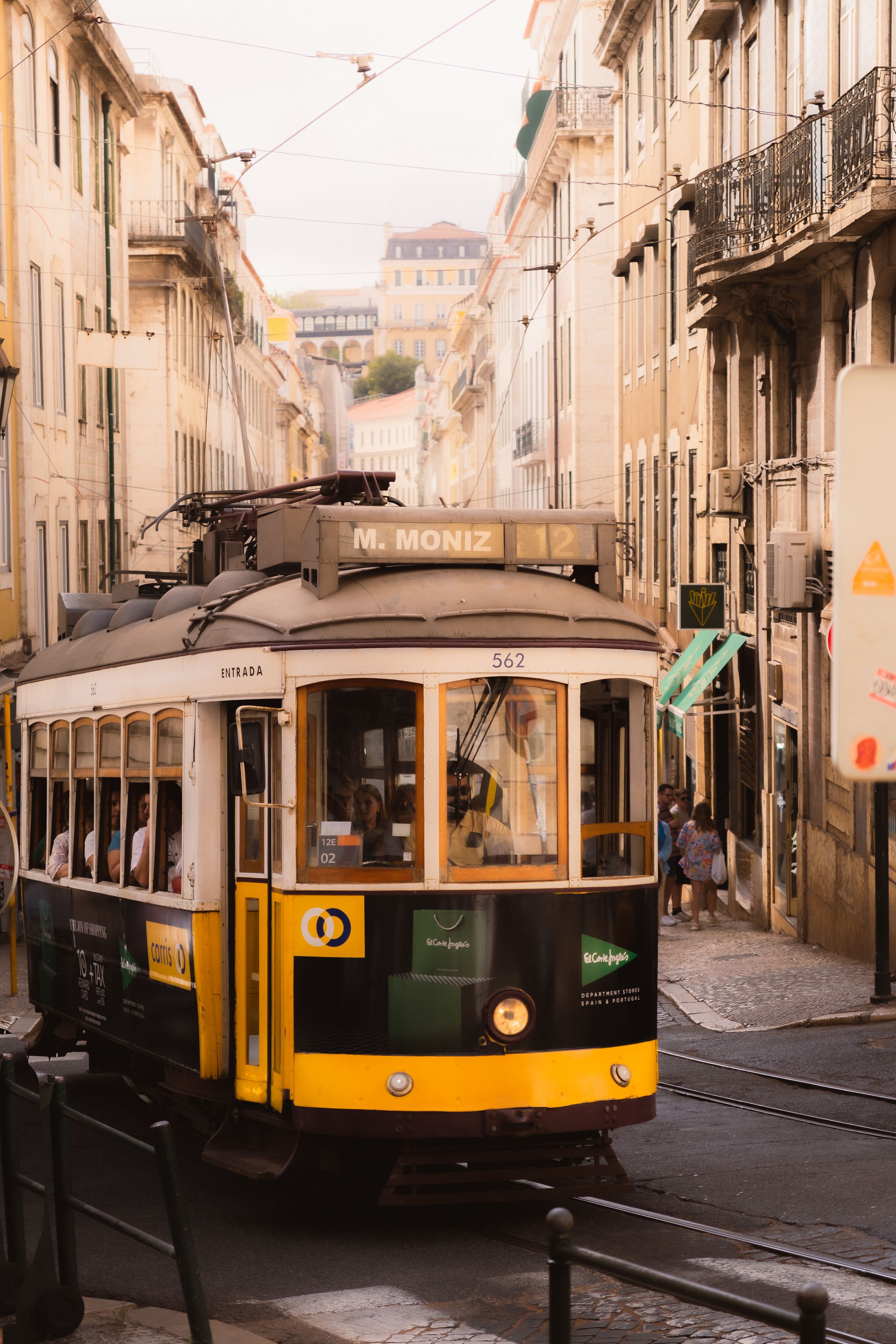 A yellow tram in the Alfama district of Lisbon on a narrow street.