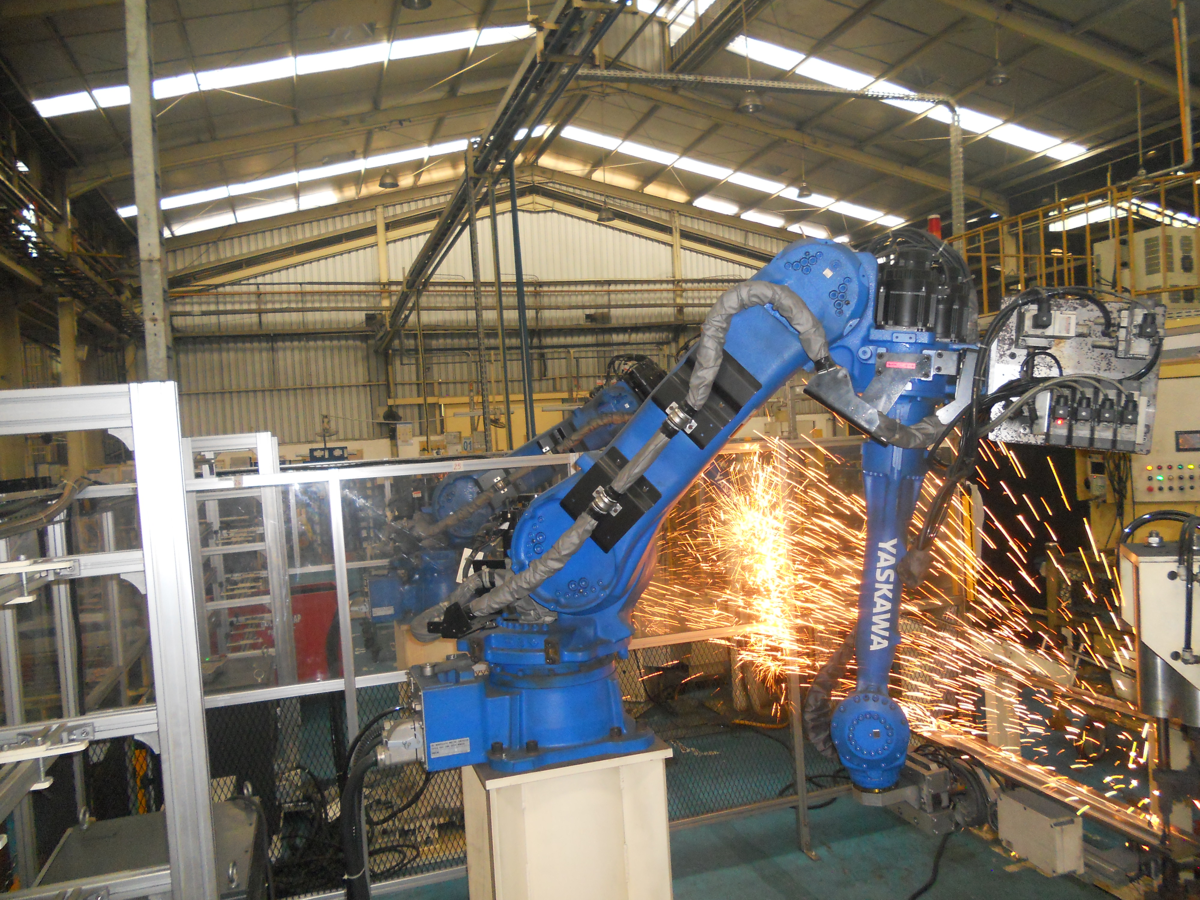 A Yaskawa industrial welding robot at work in a factory, with sparks from the weld.
