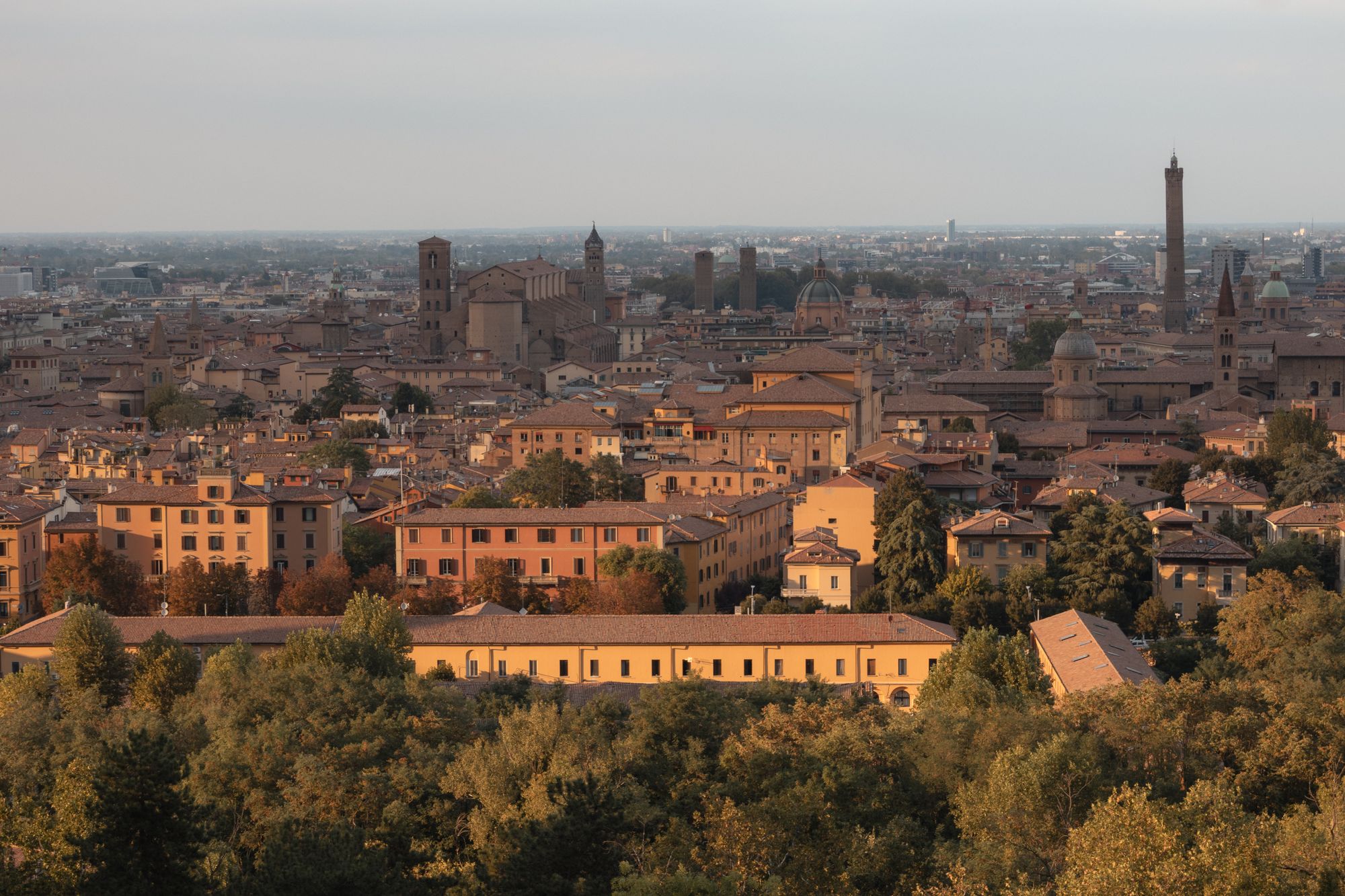 An aerial view of Bologna's historic centre at dusk with its towers and terracotta roofs.