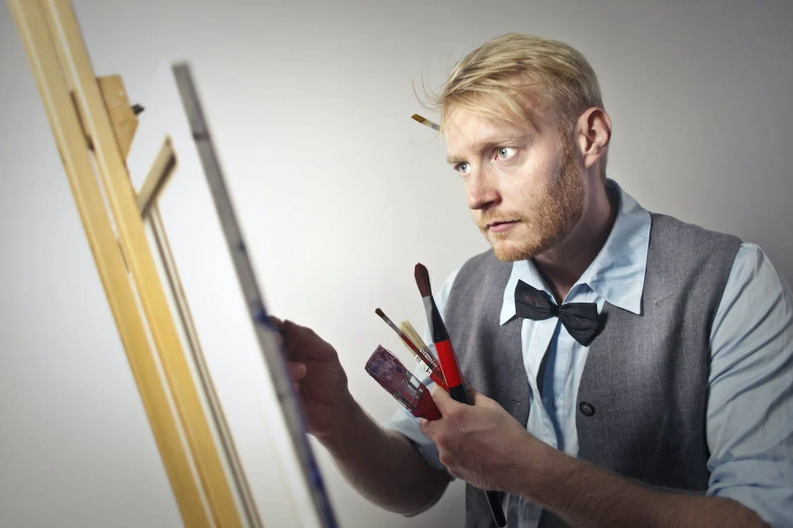 Calm male artist painting on canvas using paintbrushes