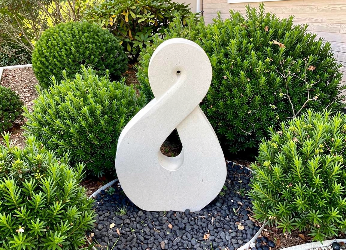 Pikorua - in garden setting with river stones - hand-carved Ōamaru limestone sculpture by Brett and Christine Keno