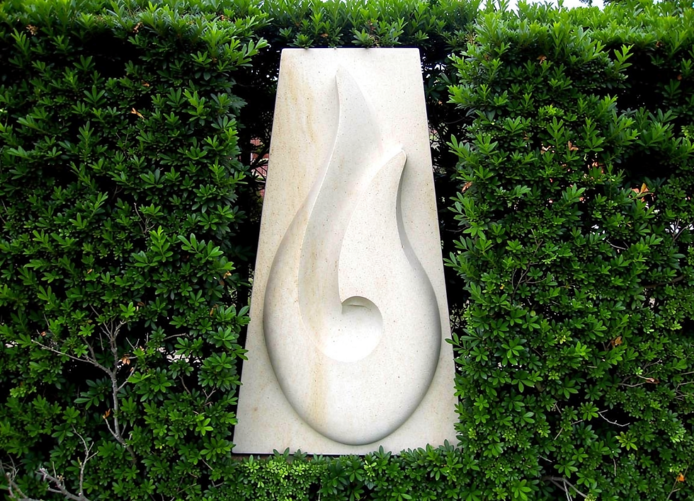 Hei Matau Wall Hanging - mounted in garden hedge - hand-carved Ōamaru limestone by Brett Keno