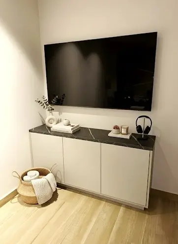 Televisor encendido sobre mueble blanco con libros y auriculares en la pared.