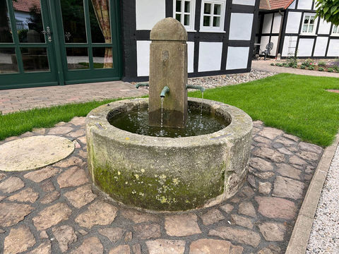 Antiker Brunnen aus Sandstein mit vier Wasserspeiern an der Säule. Runder Brunnen. Alter Brunnen, historisches Sammlerstück.