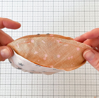 Two hands show a 2 inch gap left after sewing two half-units of a fabric basketball together