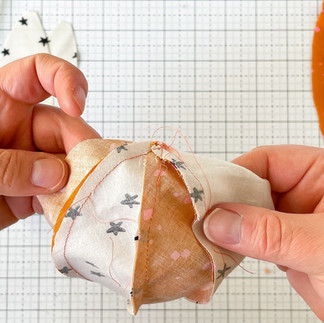 Two hands hold a previously sewn unit of four pieces of fabric showing the seams going in the same direction