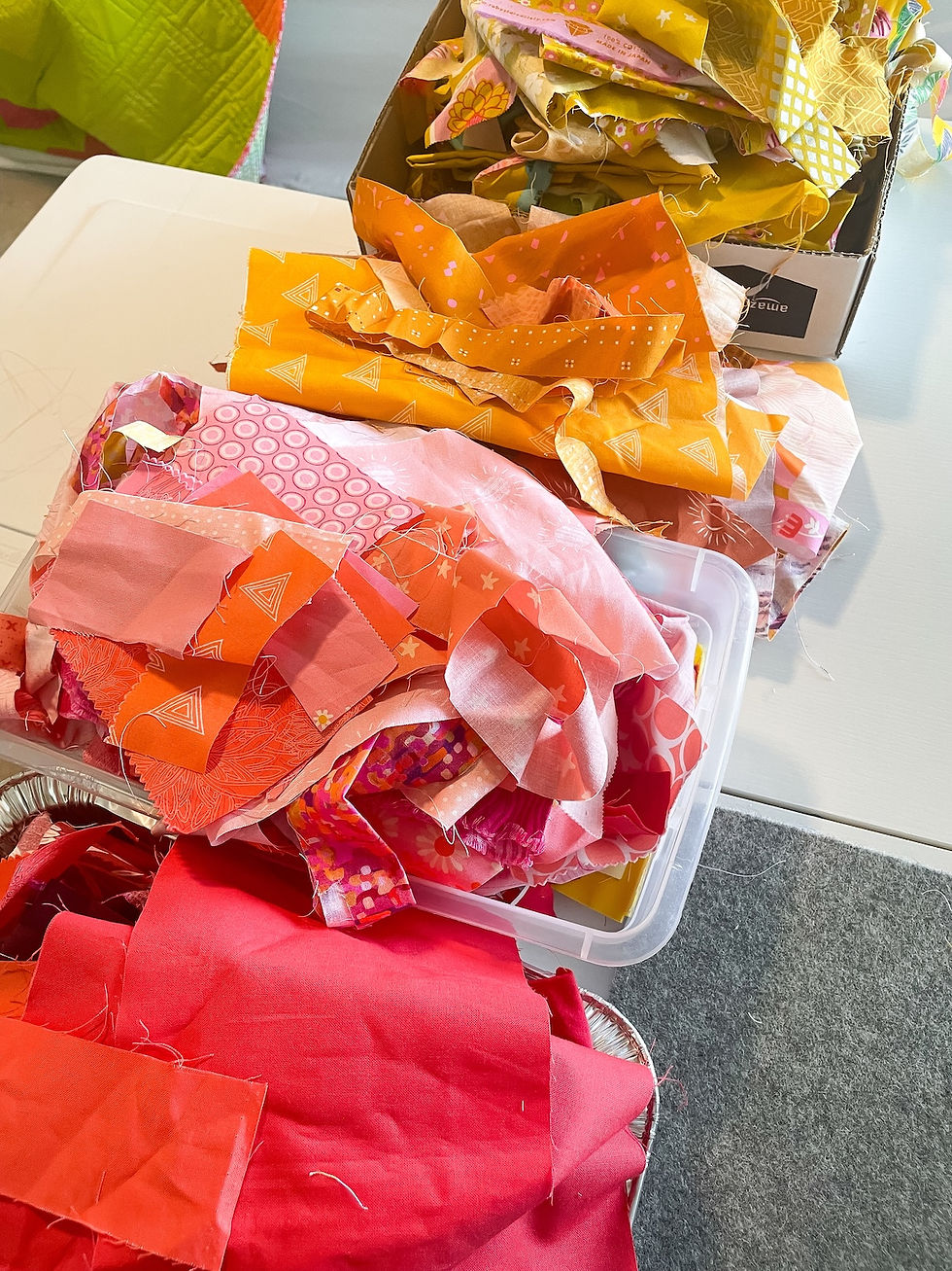 Scraps of red, pink, orange and yellow fabrics sit organized by color in bins on a white table