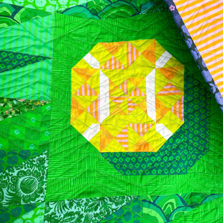 A close up of a multi-colored green quilt with a yellow and orange tennis ball block.
