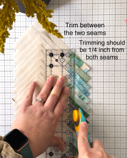 Hands trimming snowballed corners of fabric using a ruler and rotary cutter with instructions on how to trim for bonus half square triangles