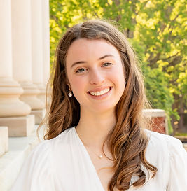 Our instructor, Miss Anna Grace, has a welcoming smile and long light-brown hair over one shoulder as she stands outdoors wearing a white blouse and dangling pearl earrings.