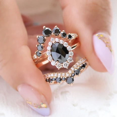Woman's hand holding rings with black gems and gold bands av luxury gems