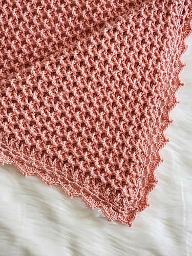 Pink knitted blanket with a waffle pattern on a white, fluffy surface.