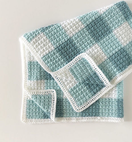 Crochet blanket with green and white checkered pattern on a light background, neatly folded, showcasing texture and design.